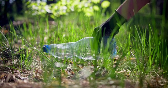 Woman picking up a plastic bottle lying on the grass while collecting trash in the forest