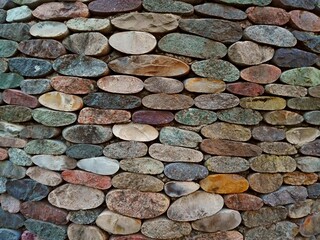 Cut pebble stone texture wall floor colorful background. Wall made from cut pebble gravel stones different shape as floor texture background. Multicolor sliced pebble cut stones wall. Cut stone wall