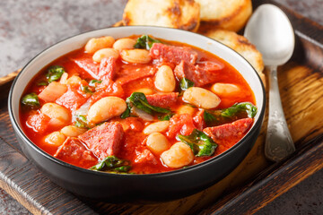 Spanish stew of butter beans, chorizo and spinach in tomato sauce close-up in a bowl on the table....