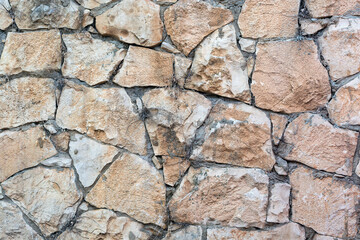 A wall built with stones of various sizes and colors, ranging from light beige to dark brown. The stones are irregular in shape and size, closely fitted together without any visible cement or mortar