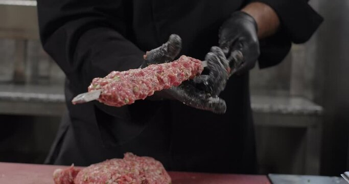 Chef shapes Turkish Adana kebab, spreads ground meat along the skewer using hands. Grilling on barbecue charcoal grill