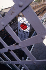 vertical image of grey crisscross metal guard rail on railway overpass walkway. red stop signage depicting danger. Location Woodbridge Railway station Suffolk UK 2003