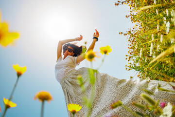 Summer mood. a young and cheerful girl posing against a background of blue sky and flowers. A beautiful girl dances among flowers. girl dancing among flowers.