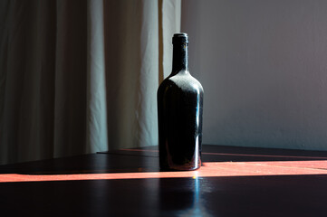 Old bottle of wine on the table in sunlight ray with dust around the neck. Wood, glass retro style decor