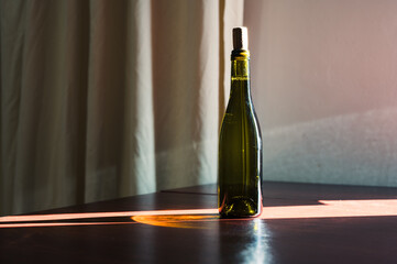 Bottle of wine with cork standing on the table. Green glass and sun ray. Style decor image
