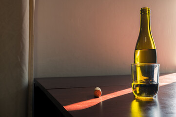 White glass and opened green bottle of wine with cork on table in sunl ray. Classic winery cellar beautiful image