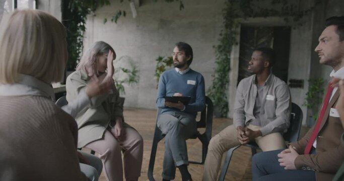 Zoom-out of psychologist working with diverse group of people talking writing report sitting in circle together. Therapy session and psychology concept.