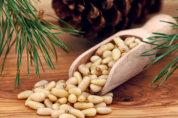 Portion of pine nuts on a scoop on an olive wood background next to a pine branch and a pine cone