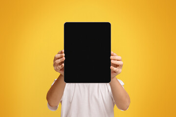 Tablet face. Little boy hiding his face behind portable computer device on orange background, free...