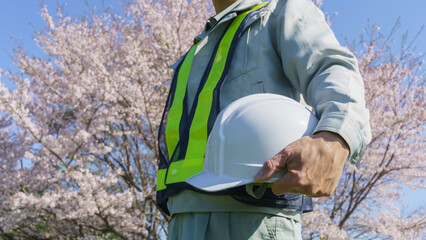 桜の花とヘルメットを持つ作業服姿の男性