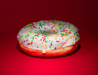 Glazed donut with sprinkles clean red background.