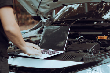 Auto mechanic inspects car by inspecting and writing checklist on laptop.