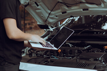 Auto mechanic inspects car by inspecting and writing checklist on laptop.