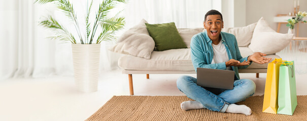 Exhilarated African American man with shopping bags and laptop, ideal for e-commerce related...