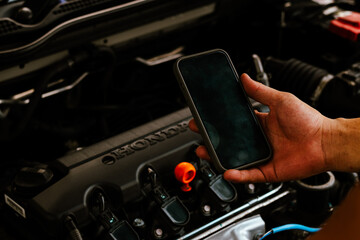 Mechanic uses smartphone to inspect car engine parts