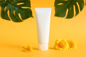 cosmetic moisturizer cream bottle tube, marigolds, tropical leaves on yellow background. Shampoo,...