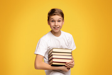 Enjoying remote education. Teen boy smiling with heap of books in hands, orange studio background