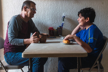 Photo of a grandfather sharing coffee and breakfast with his grandson at a plastic table with a...