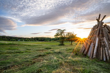 Holzstapel für Sonnenwendfeuer im Sonnenuntergang mit der untergehenden Sonne