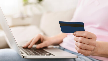 Cropped of woman sitting at a desk is holding a credit card in one hand and using a laptop with the...