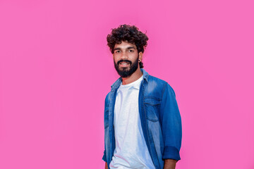 Young indian man wearing blue denim shirt standing over isolated pink background with hands together and crossed fingers smiling relaxed and cheerful