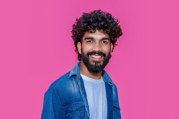 Smiling cheerful young curly bearded indian cool positive guy laughing isolated on pink background. Happy ethnic man looking at camera having fun posing for head shot close up face portrait.