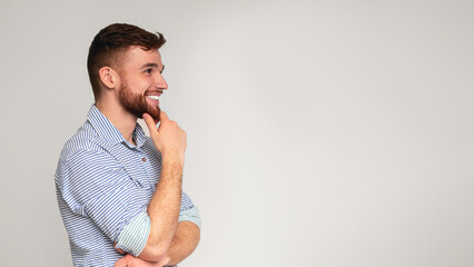 Young smiling man thinking and looking away on free space on studio background, panorama, free space