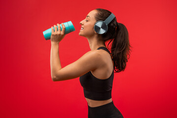 A woman wearing headphones is holding a blue cup to her lips, taking a sip of a beverage. She...