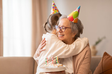 A tender moment captured as an older woman embraces a young girl, both wearing celebratory birthday...