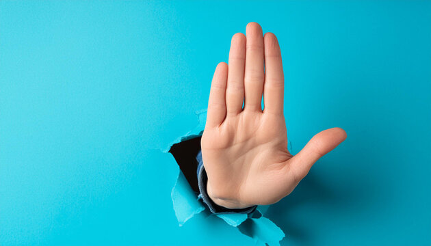 Hand making a stop sign, coming out of a torn blue paper hole. Concept of stop