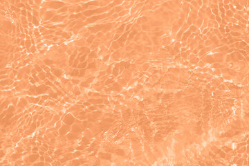 Orange water with ripples on the surface. Defocus blurred transparent orange colored clear calm water surface texture with splashes and bubbles. Water waves with shining pattern texture background.