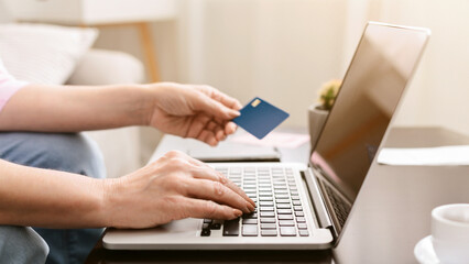 Lady holding a credit card in one hand while operating a laptop with the other hand, focused on...