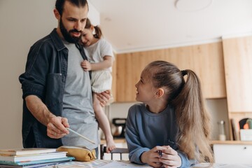 first grade girl doing her homework with her father and younger sister at home at the kitchen table