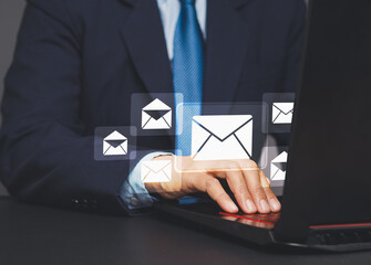 Businessman using a laptop receives a new message with email icons while sitting at the table.