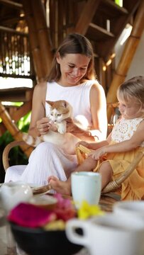 Mother and cild having breakfast in bamboo house tropical resort and playing with cat