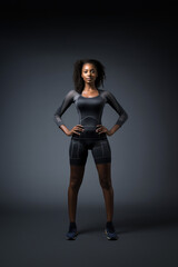 A beautiful ebony model in a sporty slim top and shorts stands on a black background with copy space.	
