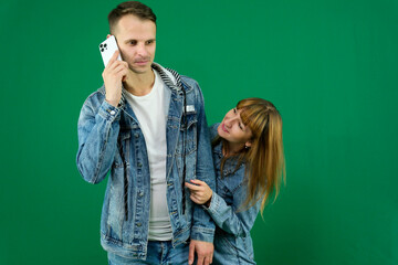 Cheerful guy and girl in denim clothes, couple, family. guy calling on the phone on a green...