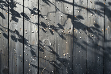 A wooden fence covered in water droplets due to dampness, surrounded by dancing shadows of trees.

