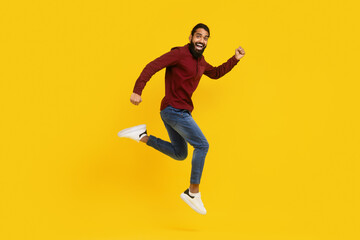 Indian man wearing a red sweater is captured mid-jump in the air. His arms are raised, and his legs...