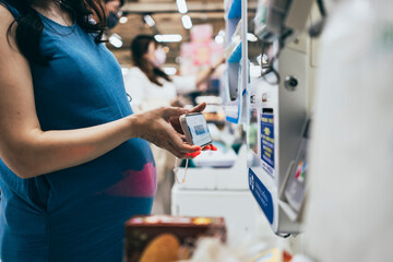 A pregnant woman checks out at the supermarket, scans a barcode, and pays electronically.