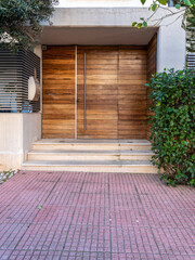 A contemporary design house entrance with a wooden door and steps by the sidewalk. Travel to Athens, Greece.