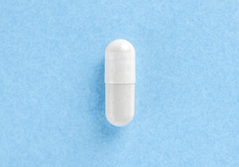 White two-piece hard starch capsule on blue background with copy space. Health concept.