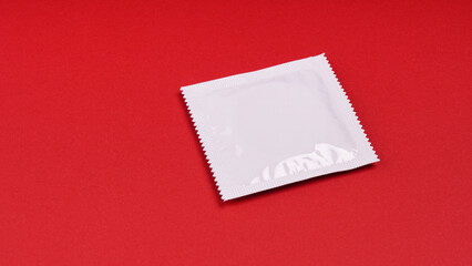 unopened white condom packet on red background with copy space