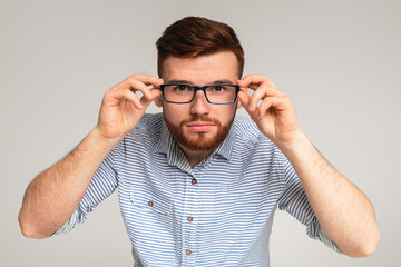 Young redhaired guy try on glasses in front of camera on studio background, panorama