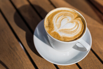Coffee on wooden background. Cup of cappuccino with latte art on brown table with sunbeam. Fresh...