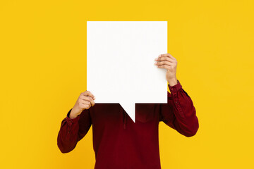 Man is shown holding a white speech bubble in front of his face. The speech bubble is blank, ready...