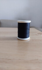 Black spool of sewing thread on wooden table.