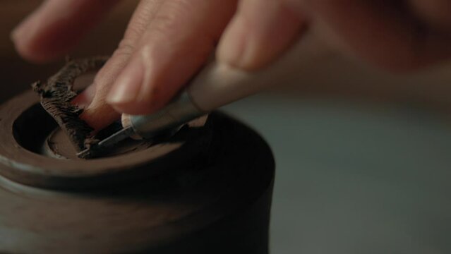 Potter scraping clay cup foot as it spins on pottery wheel