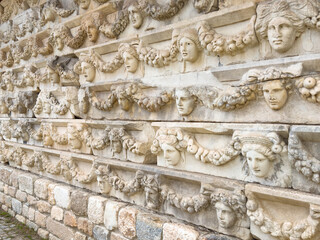 Close-up of a detailed frieze in Aphrodisias, Turkey, displaying an array of classical faces and intricate garland designs. - obrazy, fototapety, plakaty