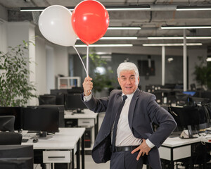 Portrait of a cheerful mature business man holding balloons in the office.